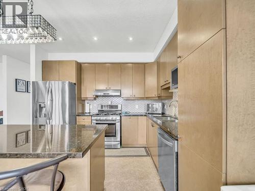 Kitchen featuring dark stone countertops, appliances with stainless steel finishes, tasteful backsplash, under cabinet range hood, and light brown cabinets - 3 Creighton Avenue, Guelph, ON - Indoor Photo Showing Kitchen