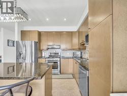 Kitchen featuring dark stone countertops, appliances with stainless steel finishes, tasteful backsplash, under cabinet range hood, and light brown cabinets - 