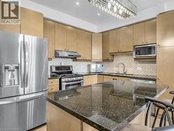 Kitchen with stainless steel appliances, dark stone counters, light brown cabinets, backsplash, and under cabinet range hood - 