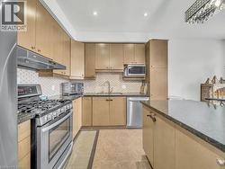 Kitchen featuring stainless steel appliances, tasteful backsplash, under cabinet range hood, dark stone countertops, and light tile patterned flooring - 