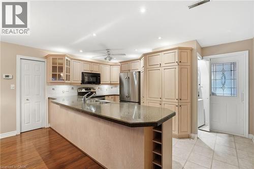Kitchen with glass insert cabinets, open shelves, a peninsula, dark stone countertops, and appliances with stainless steel finishes - 3230 New Street Unit# 7, Burlington, ON - Indoor Photo Showing Kitchen With Double Sink