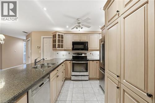 Kitchen featuring glass insert cabinets, appliances with stainless steel finishes, light brown cabinets, ceiling fan, and dark stone counters - 3230 New Street Unit# 7, Burlington, ON - Indoor Photo Showing Kitchen With Double Sink