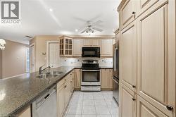 Kitchen featuring glass insert cabinets, appliances with stainless steel finishes, light brown cabinets, ceiling fan, and dark stone counters - 