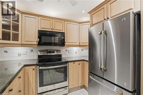 Kitchen featuring stainless steel appliances, backsplash, glass insert cabinets, dark stone countertops, and light brown cabinets - 3230 New Street Unit# 7, Burlington, ON - Indoor Photo Showing Kitchen