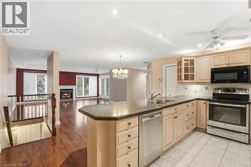 Kitchen with stainless steel appliances, glass insert cabinets, light brown cabinets, open floor plan, and a peninsula - 3230 New Street Unit# 7, Burlington, ON - Indoor Photo Showing Kitchen With Double Sink