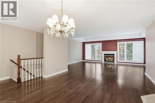 Unfurnished living room featuring dark wood finished floors, a glass covered fireplace, and a chandelier - 3230 New Street Unit# 7, Burlington, ON - Indoor With Fireplace