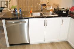 Kitchen featuring stainless steel dishwasher, white cabinetry, and light wood-type flooring - 