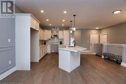 Kitchen with sink, hanging light fixtures, white cabinets, a center island with sink, and wall chimney exhaust hood - 