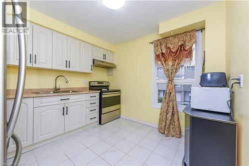 Kitchen featuring appliances with stainless steel finishes, under cabinet range hood, white cabinets, light countertops, and light tile patterned floors - 85 Enmount Drive, Brampton, ON - Indoor Photo Showing Kitchen With Double Sink