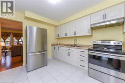 Kitchen with stainless steel appliances, under cabinet range hood, white cabinetry, and light tile patterned flooring - 