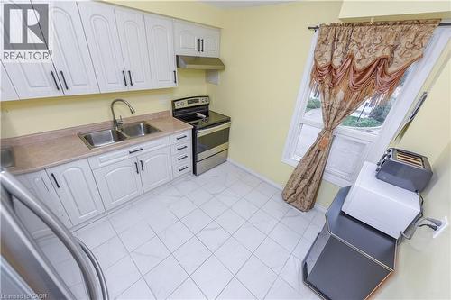 Kitchen featuring stainless steel appliances, white cabinets, light countertops, under cabinet range hood, and light tile patterned flooring - 85 Enmount Drive, Brampton, ON - Indoor Photo Showing Kitchen With Double Sink