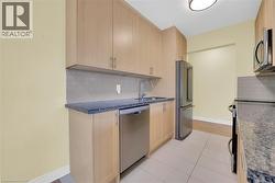 Kitchen featuring light brown cabinets, tasteful backsplash, dark Granite countertops, stainless steel appliances, and light tile patterned floors - 