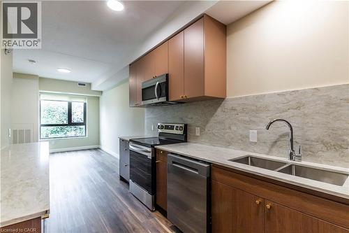 Kitchen featuring stainless steel appliances, backsplash, light stone counters, and dark wood finished floors - 580 Coldstream Drive Unit# 212, Waterloo, ON - Indoor Photo Showing Kitchen With Double Sink