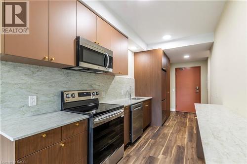 Kitchen featuring stainless steel appliances, dark wood-style flooring, decorative backsplash, light stone countertops, and modern cabinets - 580 Coldstream Drive Unit# 212, Waterloo, ON - Indoor Photo Showing Kitchen With Stainless Steel Kitchen