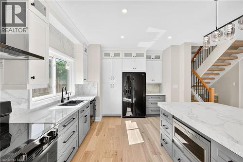 Kitchen featuring gray cabinetry, light stone counters, pendant lighting, appliances with stainless steel finishes, and ventilation hood - 4006 Flemish Drive, Burlington, ON - Indoor Photo Showing Kitchen With Double Sink