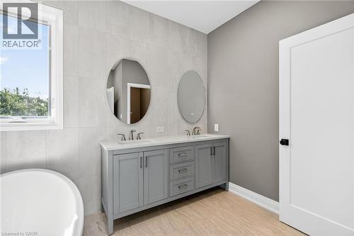 Bathroom featuring tile walls, a freestanding bath, double vanity, and light wood-style flooring - 4006 Flemish Drive, Burlington, ON - Indoor Photo Showing Bathroom