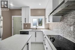 Kitchen with wall chimney exhaust hood, black electric cooktop, white cabinetry, dishwashing machine, and double oven - 