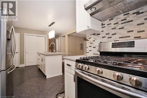 Kitchen featuring stainless steel appliances, white cabinets, premium range hood, pendant lighting, and a center island with sink - 61 Bosworth Crescent, Kitchener, ON - Indoor Photo Showing Kitchen