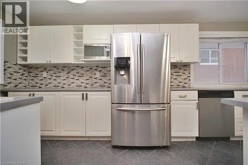 Kitchen featuring appliances with stainless steel finishes, white cabinetry, open shelves, dark tile patterned floors, and backsplash - 61 Bosworth Crescent, Kitchener, ON - Indoor Photo Showing Kitchen