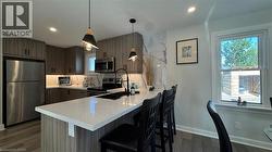 Kitchen with stainless steel appliances, hanging light fixtures, a kitchen bar, a peninsula, and dark wood finished floors - 