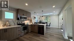 Kitchen featuring stainless steel appliances, a peninsula, decorative light fixtures, backsplash, and modern cabinets - 