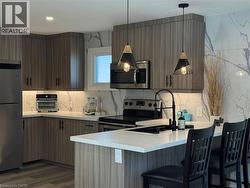 Kitchen featuring stainless steel appliances, a breakfast bar area, a peninsula, pendant lighting, and light stone countertops - 