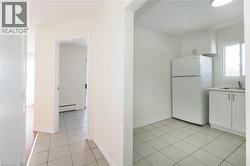 Kitchen with white cabinets, freestanding refrigerator, light countertops, a baseboard heating unit, and light tile patterned floors - 