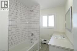 Bathroom with tub / shower combination, vanity, a baseboard heating unit, and light tile patterned floors - 