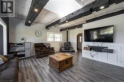 Living area featuring wainscoting, a wood stove, a decorative wall, dark wood-style flooring, and beam ceiling - 