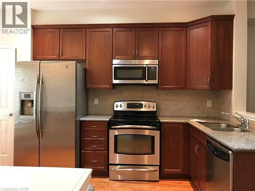 Kitchen featuring appliances with stainless steel finishes, light stone countertops, tasteful backsplash, and light wood-type flooring - 4294 Ingram Common, Burlington, ON - Indoor Photo Showing Kitchen With Stainless Steel Kitchen With Double Sink