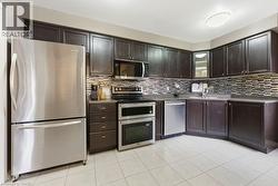 Kitchen featuring appliances with stainless steel finishes, light tile patterned floors, glass insert cabinets, tasteful backsplash, and dark brown cabinetry - 