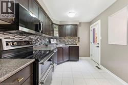 Kitchen featuring stainless steel appliances, dark brown cabinetry, glass insert cabinets, decorative backsplash, and light tile patterned flooring - 