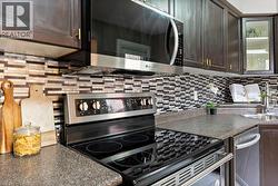 Kitchen featuring dark countertops, stainless steel appliances, dark brown cabinets, tasteful backsplash, and glass insert cabinets - 