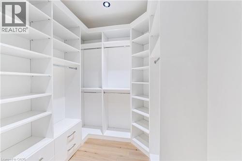 One of two walk-in closets in the primary bedroom with custom white cabinetry, luxury flooring - 515 Hamilton Drive, Ancaster, ON - Indoor With Storage