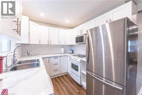 Kitchen featuring appliances with stainless steel finishes, white cabinetry, dark wood finished floors, tasteful backsplash, and light stone countertops - 140 Royal Avenue, Hamilton, ON - Indoor Photo Showing Kitchen With Double Sink With Upgraded Kitchen