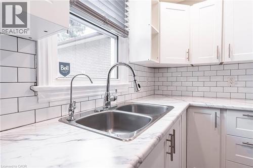 Kitchen featuring white cabinetry, decorative backsplash, and light stone counters - 140 Royal Avenue, Hamilton, ON - Indoor Photo Showing Kitchen With Double Sink