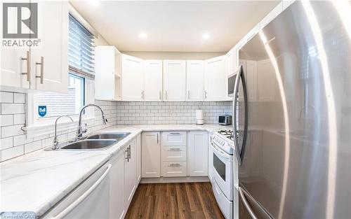 Kitchen featuring appliances with stainless steel finishes, white cabinetry, dark wood-type flooring, light stone counters, and decorative backsplash - 140 Royal Avenue, Hamilton, ON - Indoor Photo Showing Kitchen With Double Sink With Upgraded Kitchen