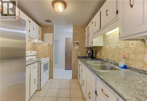 Kitchen with freestanding refrigerator, electric range, light tile patterned flooring, under cabinet range hood, and white cabinets - 4 Avalon Place Unit# 103, Kitchener, ON - Indoor Photo Showing Kitchen With Double Sink