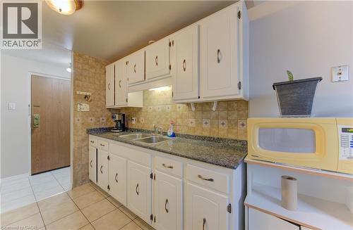 Kitchen with white cabinetry, light tile patterned floors, and tasteful backsplash - 4 Avalon Place Unit# 103, Kitchener, ON - Indoor Photo Showing Kitchen With Double Sink