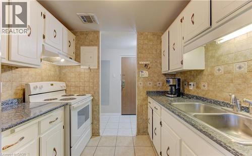 Kitchen with white range with electric stovetop, under cabinet range hood, light tile patterned floors, and white cabinetry - 4 Avalon Place Unit# 103, Kitchener, ON - Indoor Photo Showing Kitchen With Double Sink