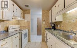 Kitchen with white range with electric stovetop, under cabinet range hood, light tile patterned floors, and white cabinetry - 