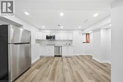 Kitchen with stainless steel appliances, light countertops, white cabinets, light wood finished floors, and recessed lighting - 