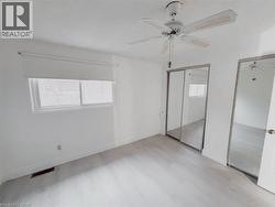 Unfurnished bedroom with two closets, multiple windows, ceiling fan, and light wood-style floors - 