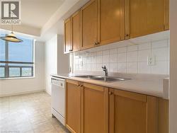 Kitchen featuring light countertops, tasteful backsplash, white dishwasher, pendant lighting, and brown cabinets - 