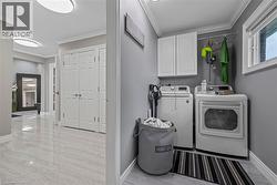 Laundry room featuring crown molding, light marble finish floors, cabinet space, and washer and dryer - 