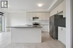 Kitchen with dark stone countertops, appliances with stainless steel finishes, a center island with sink, under cabinet range hood, and light tile patterned flooring - 