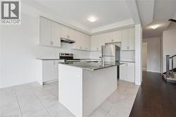 Kitchen with dark stone countertops, stainless steel appliances, an island with sink, under cabinet range hood, and light tile patterned flooring - 