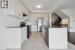 Kitchen with appliances with stainless steel finishes, dark stone counters, a center island with sink, under cabinet range hood, and light tile patterned floors - 