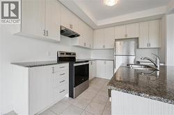 Kitchen with dark stone counters, stainless steel appliances, under cabinet range hood, and light tile patterned floors - 