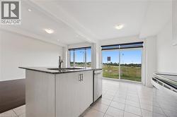 Kitchen featuring dark stone counters, light tile patterned floors, a center island with sink, white cabinets, and stainless steel appliances - 